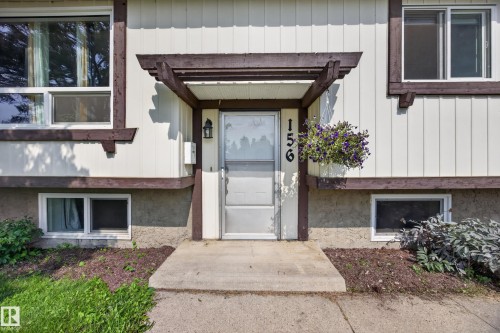 Welcoming entry featuring a covered pergola-style overhang with wood-finish trim, frosted-glass storm door with sidelights, and manicured landscaping with mulch beds and mature plantings flanking the approach - 156 Clareview Road Nw, Edmonton, AB - Outdoor With Exterior