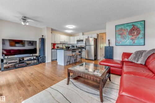 Open-concept living space featuring hardwood flooring throughout, a red leather sectional sofa, and a wood-frame coffee table - 3032 31 Avenue Nw, Edmonton, AB - Indoor Photo Showing Living Room