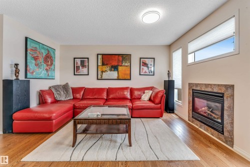 Warm living space featuring wood-finish flooring, a contemporary fireplace with a stone surround, and multiple windows providing natural light - 3032 31 Avenue Nw, Edmonton, AB - Indoor Photo Showing Living Room With Fireplace