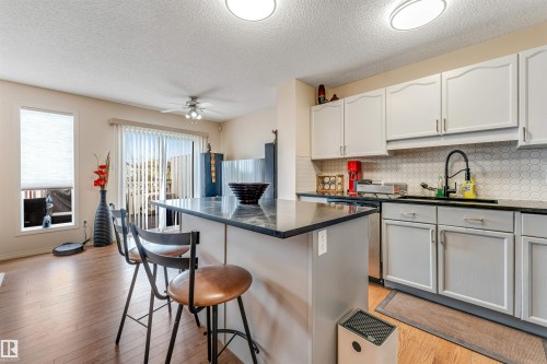 Kitchen featuring light-toned cabinetry, dark countertops, a white hexagonal tile backsplash, and wood-finish flooring - 3032 31 Avenue Nw, Edmonton, AB - Indoor Photo Showing Kitchen
