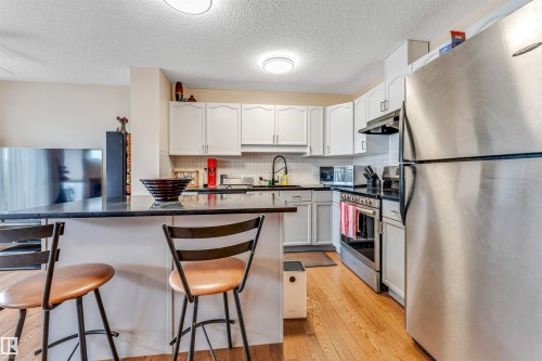 Kitchen featuring white cabinetry, dark countertops, a tile backsplash, stainless steel appliances, and wood-finish flooring - 3032 31 Avenue Nw, Edmonton, AB - Indoor Photo Showing Kitchen
