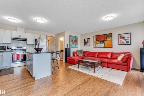 Open-concept living area with wood-finish flooring, recessed lighting, white cabinetry, a kitchen island with seating, and stainless steel appliances - 3032 31 Avenue Nw, Edmonton, AB - Indoor