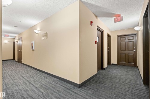 Hallway with neutral-toned walls, gray patterned carpeting, and multiple entry doors - #404 11103 84 Av Nw, Edmonton, AB - Indoor Photo Showing Other Room