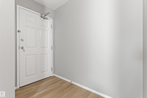 Entryway featuring a paneled door with polished hardware, light gray walls, and wood-finish flooring - #404 11103 84 Av Nw, Edmonton, AB - Indoor Photo Showing Other Room