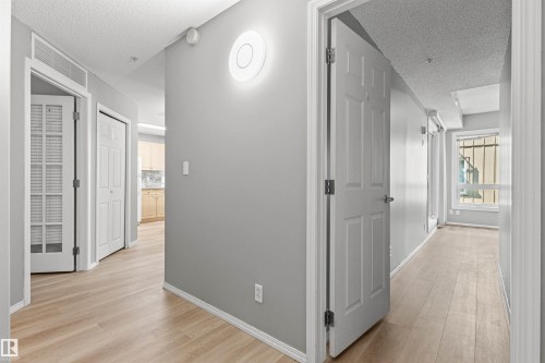 Wood-finish flooring throughout, smooth white panel doors, wall-mounted light fixture, and white baseboards - #404 11103 84 Av Nw, Edmonton, AB - Indoor Photo Showing Other Room