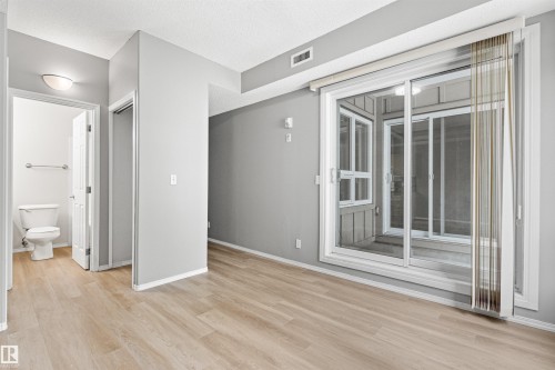 Wood-finish flooring throughout, light gray wall paint, and a sliding glass door - #404 11103 84 Av Nw, Edmonton, AB - Indoor Photo Showing Other Room