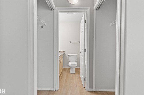 Bathroom featuring a white toilet, light wood-finish flooring, wood vanity with a stone countertop, and a towel bar - #404 11103 84 Av Nw, Edmonton, AB - Indoor Photo Showing Bathroom