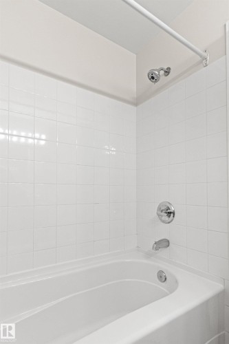 White ceramic tile surround with chrome shower fixtures and a white acrylic bathtub - #404 11103 84 Av Nw, Edmonton, AB - Indoor Photo Showing Bathroom