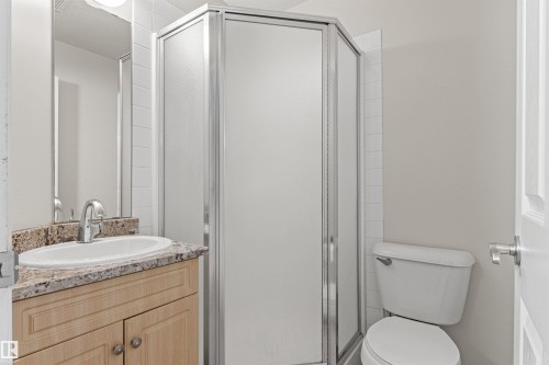 Compact bathroom featuring a shower enclosure with frosted panels, a built-in vanity with a granite-look countertop, an integrated sink with a chrome faucet, and a white toilet - #404 11103 84 Av Nw, Edmonton, AB - Indoor Photo Showing Bathroom