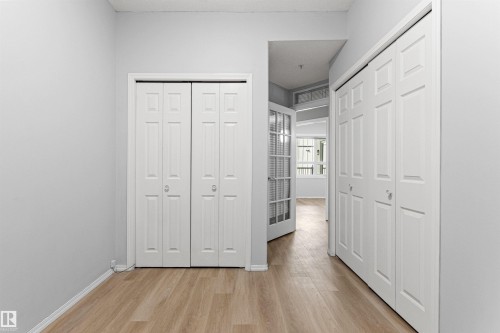 Wood-finish flooring, white bi-fold closet doors, and a white French door with frosted glass panels - #404 11103 84 Av Nw, Edmonton, AB - Indoor Photo Showing Other Room