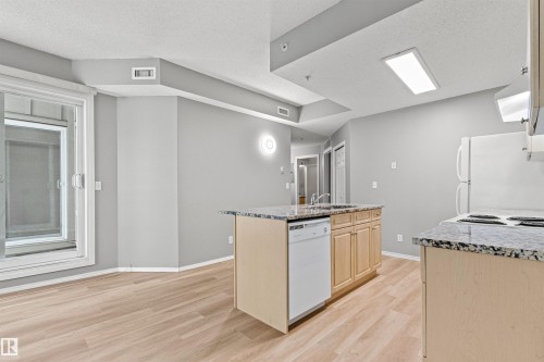 Kitchen featuring an island with a built-in sink, dishwasher, and granite-style countertop - #404 11103 84 Av Nw, Edmonton, AB - Indoor Photo Showing Kitchen