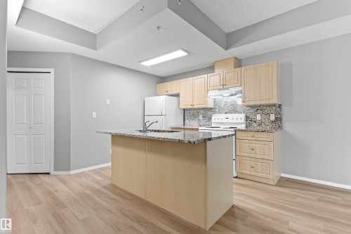 Kitchen featuring wood-finish cabinetry, granite countertops, an island with a sink, and wood-finish flooring - #404 11103 84 Av Nw, Edmonton, AB - Indoor Photo Showing Kitchen