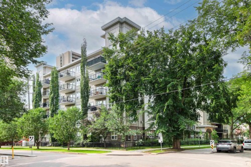 Multi-story building featuring numerous private balconies with black railings, a light-colored exterior, and surrounding mature trees - #404 11103 84 Av Nw, Edmonton, AB - Outdoor With Balcony