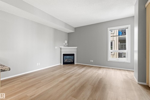Spacious living area featuring wood-finish flooring, a white mantel, and an electric fireplace insert - #404 11103 84 Av Nw, Edmonton, AB - Indoor Photo Showing Living Room With Fireplace