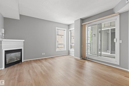 Living area with wood-finish flooring, a white mantel fireplace, and sliding glass doors - #404 11103 84 Av Nw, Edmonton, AB - Indoor Photo Showing Living Room With Fireplace