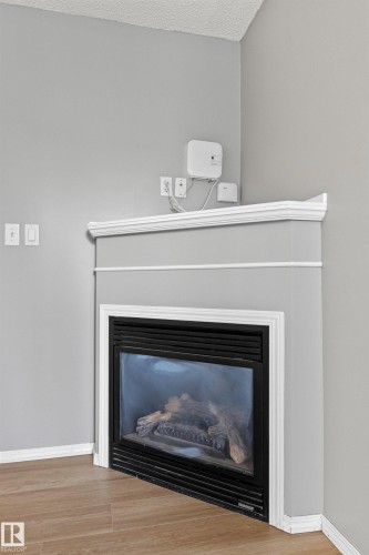 Corner fireplace with a mantel, crown molding, and wood-finish flooring - #404 11103 84 Av Nw, Edmonton, AB - Indoor Photo Showing Living Room With Fireplace
