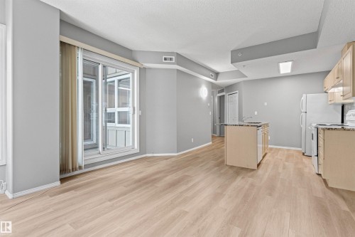 Open-concept living space featuring wood-finish flooring, a kitchen island with granite-style countertop, light wood cabinetry, and a sliding glass door to an enclosed balcony - #404 11103 84 Av Nw, Edmonton, AB - Indoor Photo Showing Kitchen