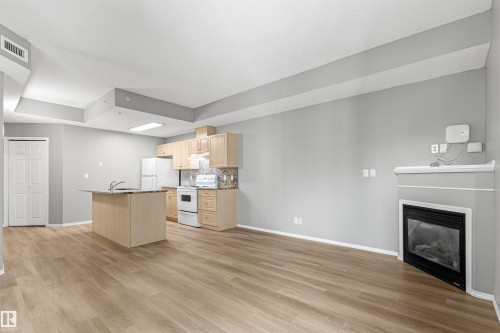 Open concept living area featuring wood-finish flooring, a kitchen island with stone countertop, light wood cabinetry, and a built-in fireplace - #404 11103 84 Av Nw, Edmonton, AB - Indoor With Fireplace