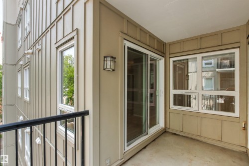 Covered outdoor living space featuring sliding glass doors, large multi-pane windows, wood-finish flooring, and neutral wall finishes with architectural panel detailing - #404 11103 84 Av Nw, Edmonton, AB -  With Exterior