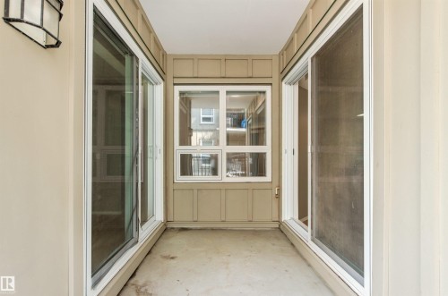 Enclosed outdoor space featuring a wall-mounted light fixture, concrete flooring, and multiple sliding glass doors - #404 11103 84 Av Nw, Edmonton, AB - Outdoor With Balcony With Exterior
