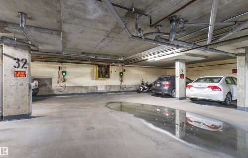 Concrete parking area featuring exposed overhead piping and multiple EV charging stations - #404 11103 84 Av Nw, Edmonton, AB - Indoor Photo Showing Garage