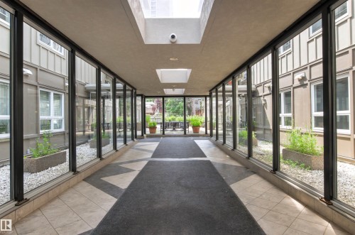 Enclosed walkway featuring full-height glazing, skylights, tiled flooring, and a landscaped courtyard with white stone and planters - #404 11103 84 Av Nw, Edmonton, AB - Indoor Photo Showing Other Room