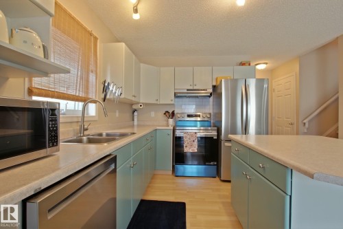 Kitchen featuring two-tone cabinetry, light-toned countertops, and stainless steel appliances - #42 4350 23 St Nw, Edmonton, AB - Indoor Photo Showing Kitchen With Double Sink