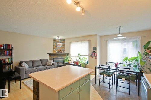 Open-concept interior featuring light wood-finish flooring, a stone-faced fireplace with a mantel, and a kitchen island with built-in cabinetry - #42 4350 23 St Nw, Edmonton, AB - Indoor With Fireplace