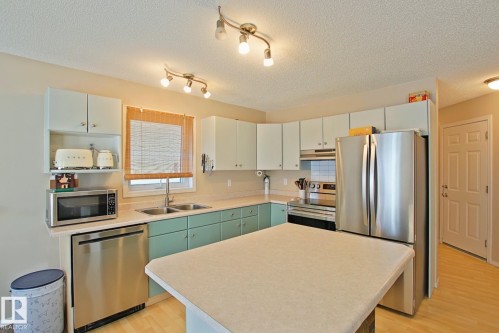 Kitchen featuring stainless steel appliances, dual-tone cabinetry, track lighting, a double basin sink, and a center island - #42 4350 23 St Nw, Edmonton, AB - Indoor Photo Showing Kitchen With Double Sink