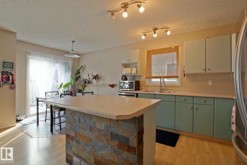 Kitchen featuring stacked stone island, light wood-finish flooring, two-tone cabinetry, and track lighting - #42 4350 23 St Nw, Edmonton, AB - Indoor Photo Showing Kitchen