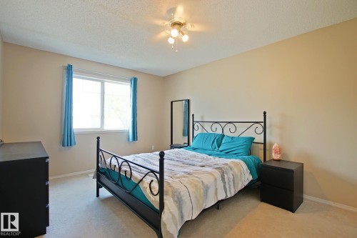 Bright secondary bedroom featuring a wrought iron bed frame, neutral carpet flooring, and soft yellow walls - #42 4350 23 St Nw, Edmonton, AB - Indoor Photo Showing Bedroom