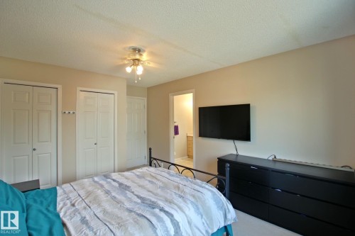 Spacious primary bedroom featuring multiple closet options, ceiling-mounted light fixture, wall-mounted flat-screen television, and black dresser with ample storage - #42 4350 23 St Nw, Edmonton, AB - Indoor Photo Showing Bedroom