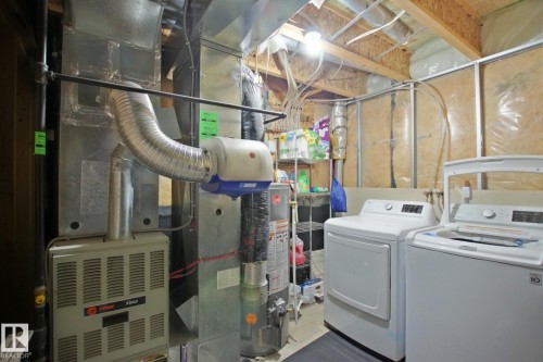 Utility area featuring exposed wood ceiling joists, HVAC system, water heater, and laundry appliances - #42 4350 23 St Nw, Edmonton, AB - Indoor