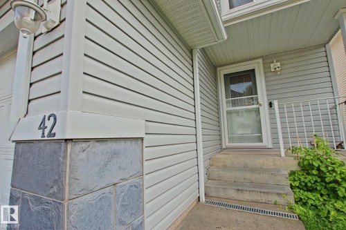 Siding exterior with decorative stone accents, concrete entry steps, and a white screen door - #42 4350 23 St Nw, Edmonton, AB - Outdoor With Exterior