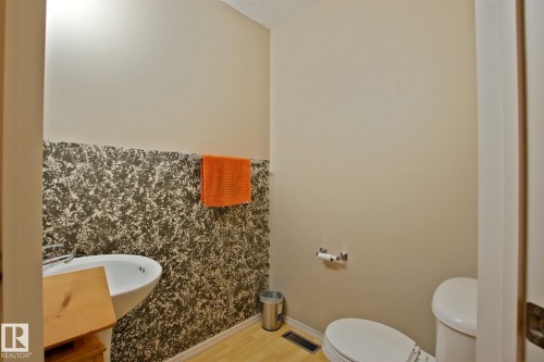 Wall-mounted sink with chrome faucet, toilet, and light wood-finish flooring - #42 4350 23 St Nw, Edmonton, AB - Indoor Photo Showing Bathroom