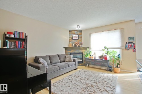 Living area featuring light-toned walls, light wood-finish flooring, and a corner fireplace with a stacked stone surround - #42 4350 23 St Nw, Edmonton, AB - Indoor Photo Showing Living Room With Fireplace