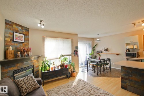 Open-concept living space featuring wood-finish flooring, a stone-clad fireplace, and a kitchen island with stone detailing - #42 4350 23 St Nw, Edmonton, AB - Indoor With Fireplace