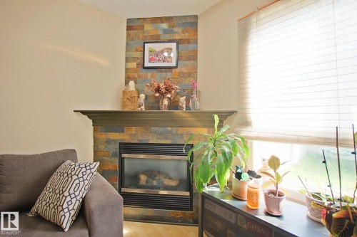 Stacked stone fireplace with a dark wood-finish mantel and a built-in gas insert - #42 4350 23 St Nw, Edmonton, AB - Indoor With Fireplace