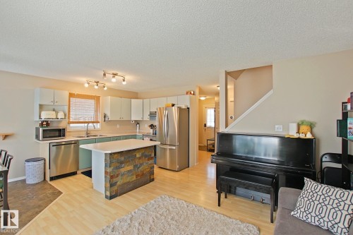 Kitchen with stainless steel appliances, light-toned cabinetry, and a central island featuring a stone-clad base and light countertop - #42 4350 23 St Nw, Edmonton, AB - Indoor Photo Showing Kitchen