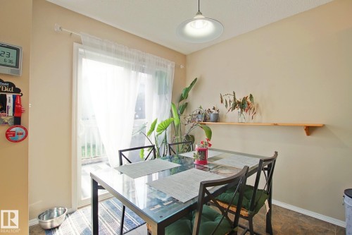 Sliding glass door with sheer white curtains, light beige wall paint, wood-finish flooring, and a built-in wood shelf - #42 4350 23 St Nw, Edmonton, AB - Indoor Photo Showing Dining Room