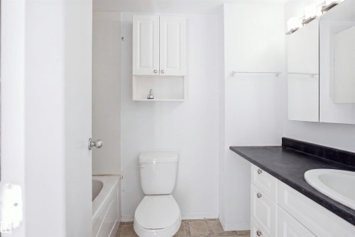 White vanity with black countertop and integrated sink, white wall-mounted medicine cabinet, toilet, and white wall-mounted storage cabinet - 7825 159 Street Nw, Edmonton, AB - Indoor Photo Showing Bathroom