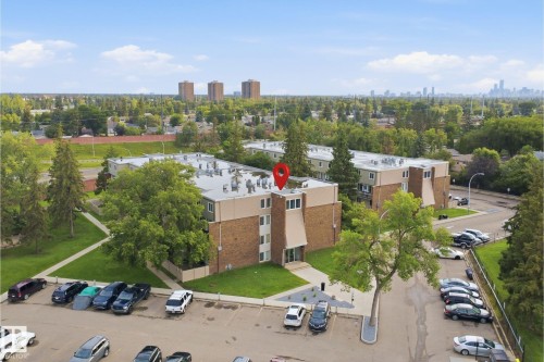 Modern brick-constructed residential building featuring a flat roofline, expansive rooftop terrace with multiple seating areas, and ample surface parking - 7825 159 Street Nw, Edmonton, AB - Outdoor With View