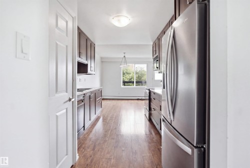 Kitchen featuring wood-finish flooring, dark wood cabinetry, stainless steel appliances, and white countertops - 7825 159 Street Nw, Edmonton, AB - Indoor Photo Showing Kitchen