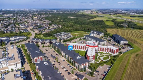 Aerial perspective showcasing residential buildings, surrounding green spaces, and a cultivated field - #315 5816 Mullen Pl Nw, Edmonton, AB - Outdoor With View