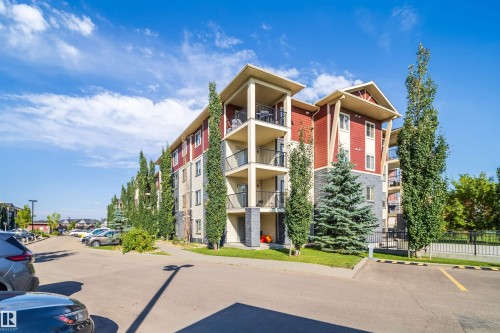 Multi-story building featuring red and beige siding, stone accents, and private balconies with black railings - #315 5816 Mullen Pl Nw, Edmonton, AB - Outdoor With Facade