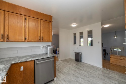 Wood cabinetry with dark hardware, stainless steel dishwasher, light gray subway tile backsplash, and light-toned, wood-finish flooring - 14215 78 Street Nw, Edmonton, AB - Indoor Photo Showing Kitchen