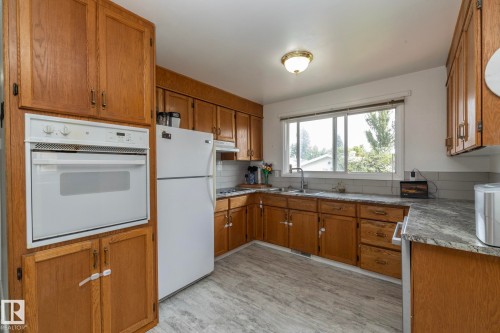 Kitchen featuring wood cabinetry, a built-in wall oven, grey subway tile backsplash, light-toned countertops, and wood-finish flooring - 14215 78 Street Nw, Edmonton, AB - Indoor Photo Showing Kitchen With Double Sink
