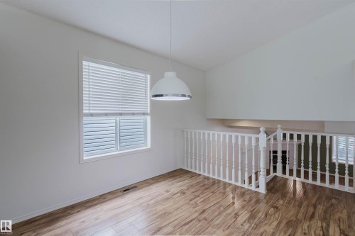 Open concept space featuring wood-finish flooring, a white spindle railing, and a vaulted ceiling - 1694 Tompkins Wynd Nw, Edmonton, AB - Indoor Photo Showing Other Room