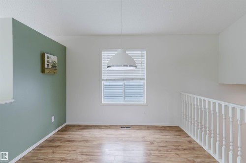 Room featuring wood-finish flooring, a window with horizontal blinds, and a contemporary pendant light fixture - 1694 Tompkins Wynd Nw, Edmonton, AB - Indoor Photo Showing Other Room