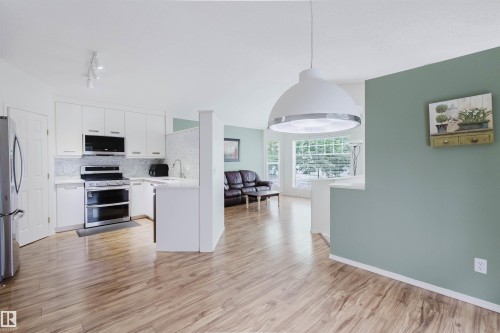 Kitchen featuring white cabinetry, stainless steel appliances, and wood-finish flooring - 1694 Tompkins Wynd Nw, Edmonton, AB - Indoor Photo Showing Kitchen